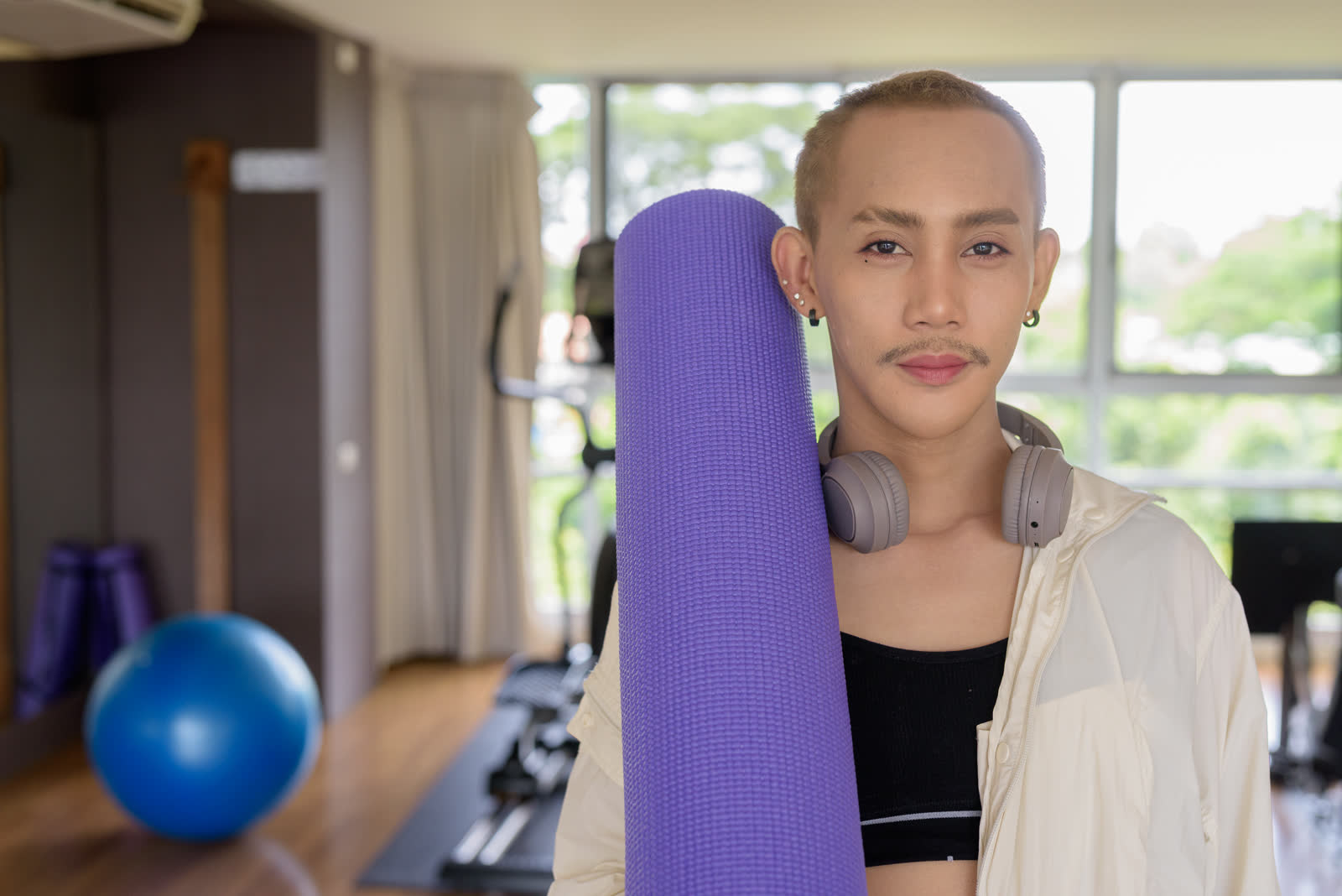 Person in a gym holding a purple yoga mat
